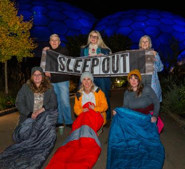 Participants at the 2024 Sleep Out in sleeping bags, holding a Sleep Out banner